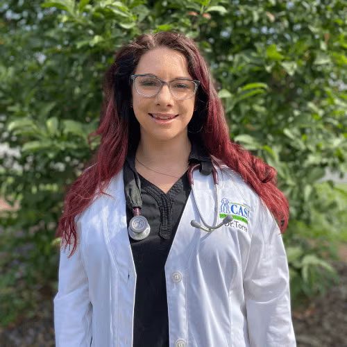 Dr. Torres smiling and posing for a photo in front of foliage
